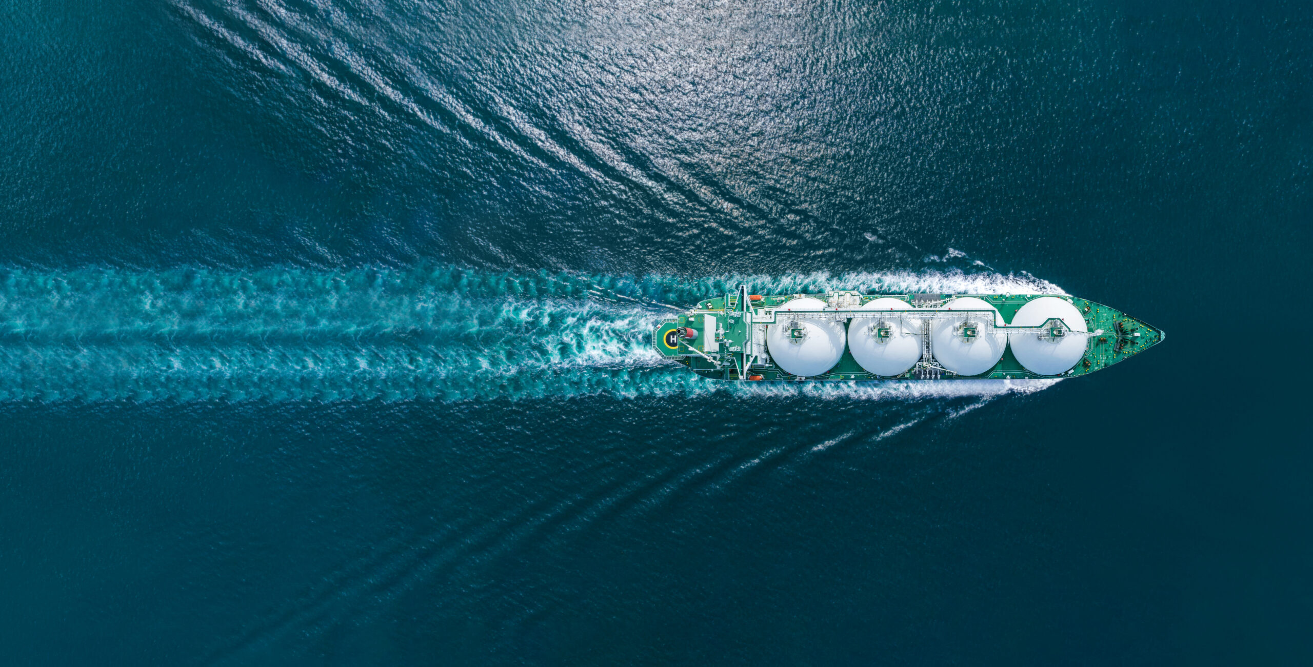 Aerial top view LNG Tanker ship (Liquified Natural Gas) with contrail in the ocean sea ship carrying container and running for export from container international port to custom ocean concept freight shipping by ship service